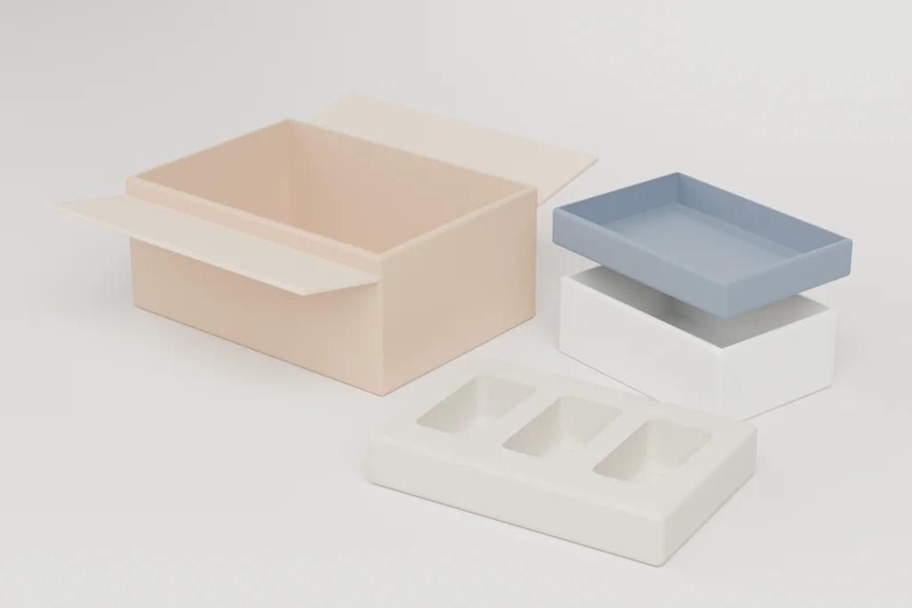 Three packaging objects on a pale surface: an open corrugated case with hinged flaps, a white moulded insert tray with three cavities, and a rigid white box with a blue lid.